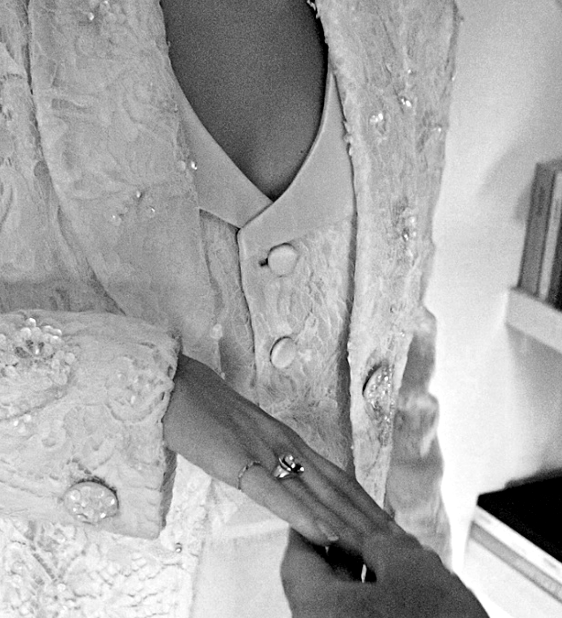 Close-up of a person wearing a decorative wedding coat with buttons and a ring on a blurred indoor background